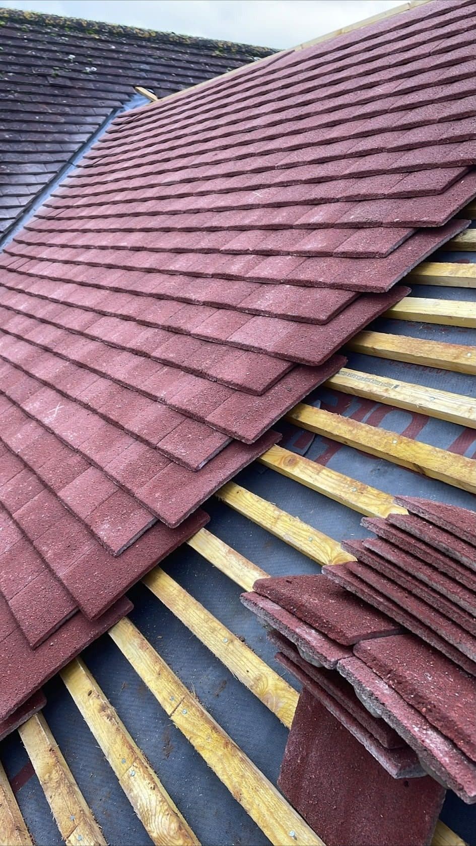 New red plain tiles being laid on new battens, with a stack of tiles waiting on the roof
